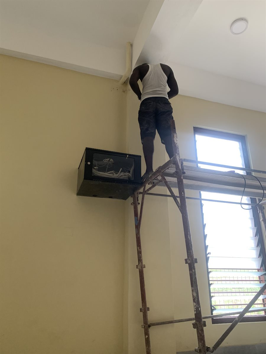 Technician installing classroom projector equipment near the ceiling.